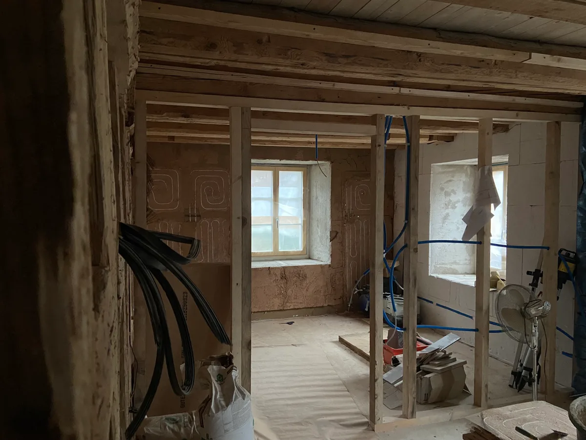 Wie im hinteren Bereich dieses Raums erkennbar ist, wird Lehm als Verputz verwendet. Dies gilt im Übrigen für den gesamten Innenbereich. Ein Innenraum einer Baustelle, wo noch viel Baumaterial herumsteht.